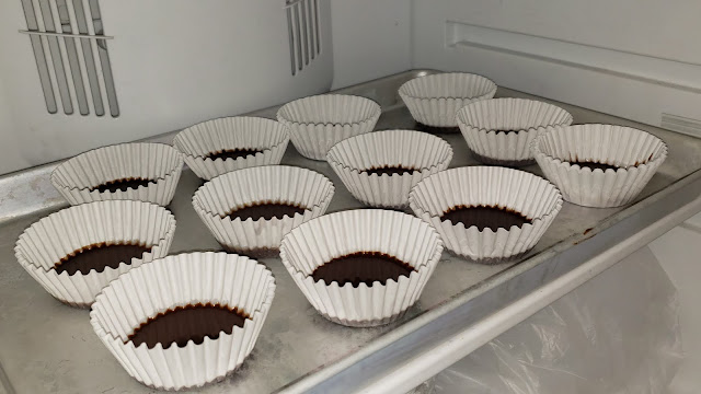 Chocolate filled cupcake liners on a baking sheet in the freezer.