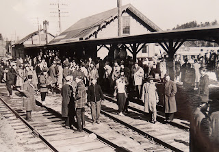 A photograph showing a crowd of figures at a train station.