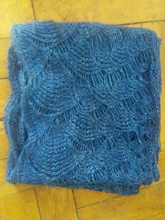 a lace scarf folded up on itself, knit in dark blue yarn. The lace is a shell motif, progressing into smalls and finally into a mesh. 