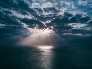 A ray of sunlight breaking through a dark sky over the ocean.