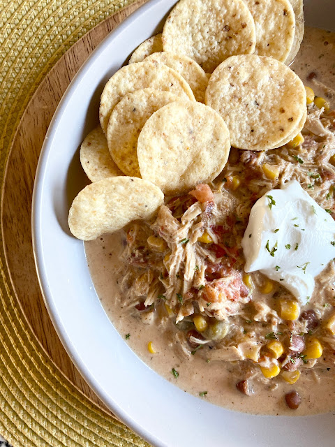 Bowl of chicken chili in a grey bowl topped with sour cream, cilantro and tortilla chips.