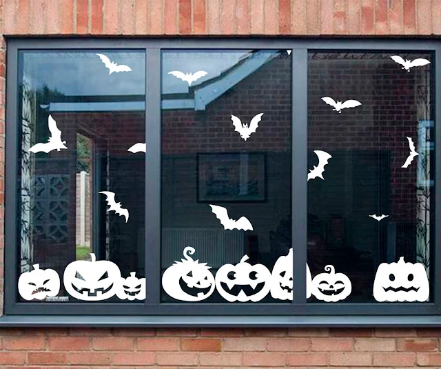 A window with white halloween window stickers in the shape of bats and pumpkins