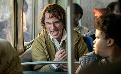 Joaquin Phoenix laughs loudly on a crowded bus in the movie Joker, directed by Todd Phillips
