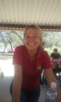 A blonde lady in a red shirt and blue jeans leaning over a table - Kim