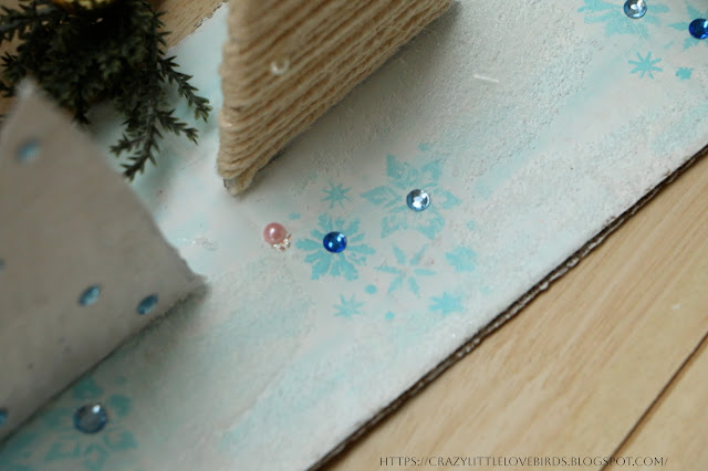 Close-up of cardboard trees, faux snow, gems, and stencil