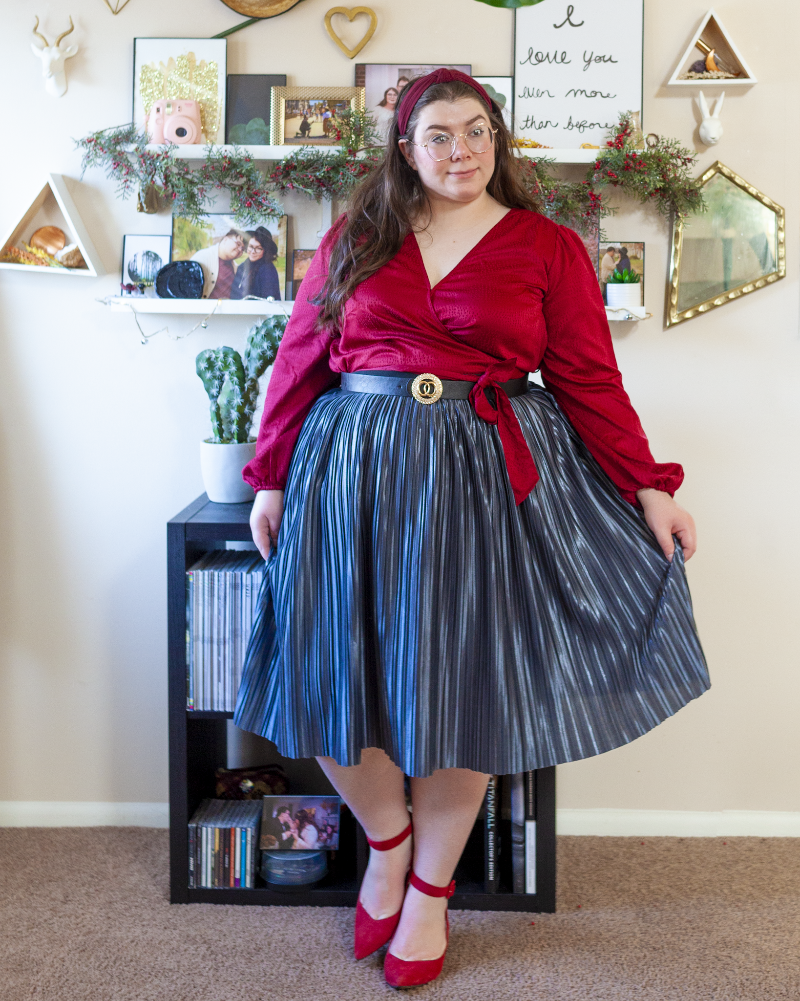 An outfit consisting of a wine red wrap top with a jacquard print over a silvery metallic pleated midi skirt and red heels.