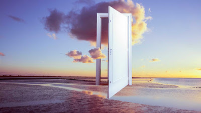 Against the backdrop of late sunset on a flat, deserted beach, covered in a shallow stretch of water, is an white door and doorframe, sitting ajar and hovering above the ground, you can see the passing, multicoloured cloud through it.