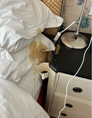 Coffee mug wedged between bed and nightstand. Coffee stains on pillows and sheets