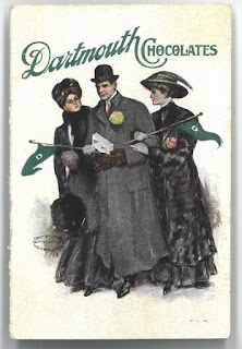 Image of Dartmouth Chocolate adversitement showing a well dressed man in an overcoat with a hat carrying a box of chocolates. There are two women, also well dressed clinging to his arm. Each woman holds a Dartmouth pennant.