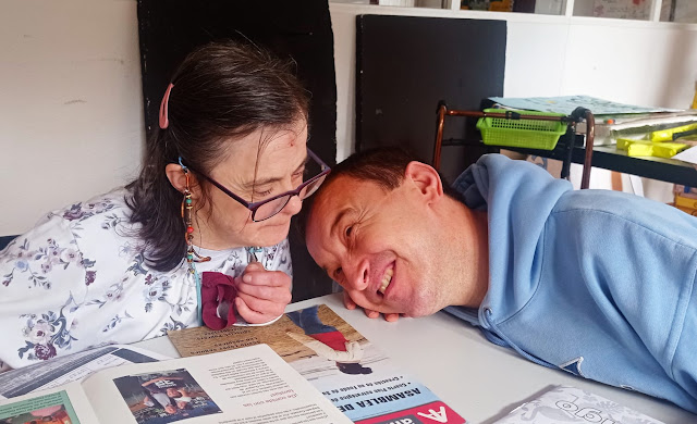 Una chica mirando una revista y un chico apoyado en la mesa mirándola