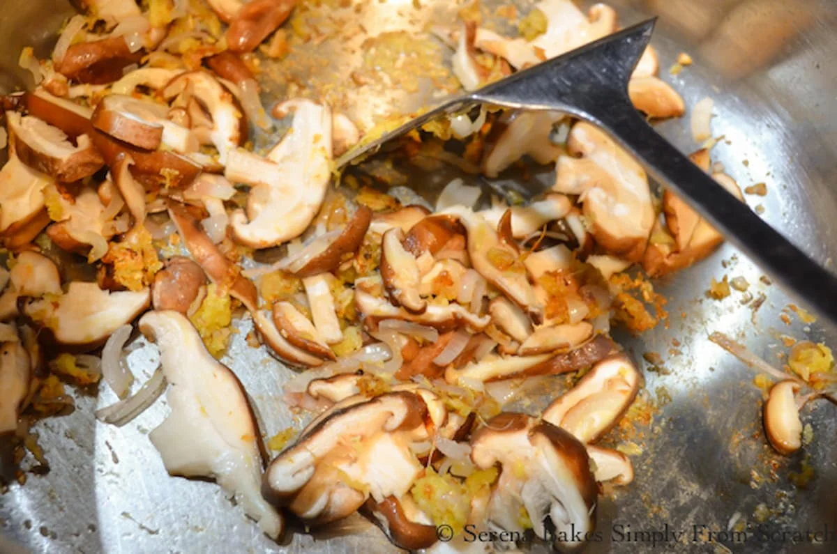 A stainless steel soup pot with olive oil, garlic, shallot ginger and shiitake mushrooms.