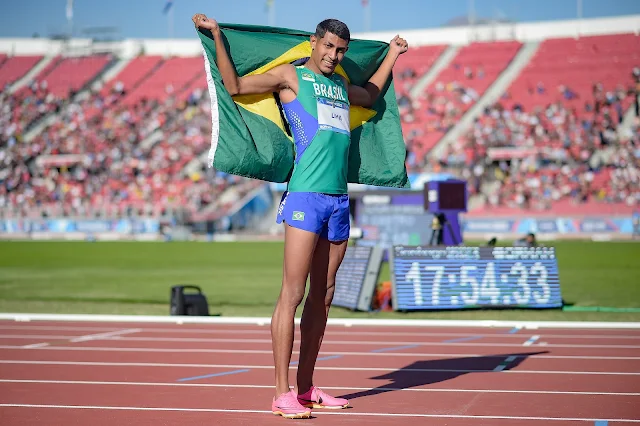 Matheus Lima está de verde, com a bandeira do Brasil nas suas costas. Ele é moreno