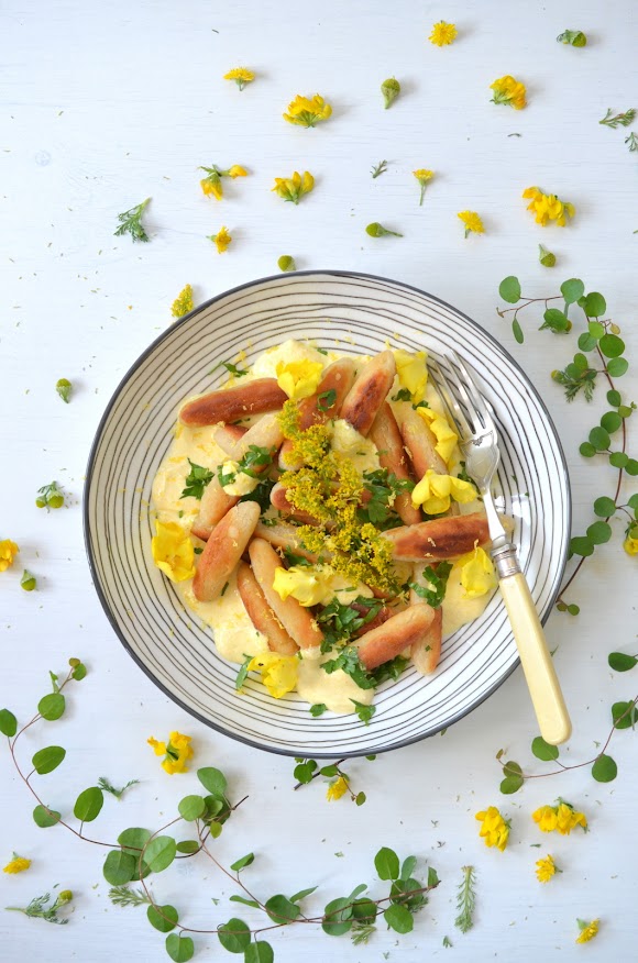 Mühlviertler Sonnwendnudeln sind auf einem Teller mit gelb gefärbter Sauerrahmcreme angerichtet und mit Blüten und gehackter Petersilie garniert.