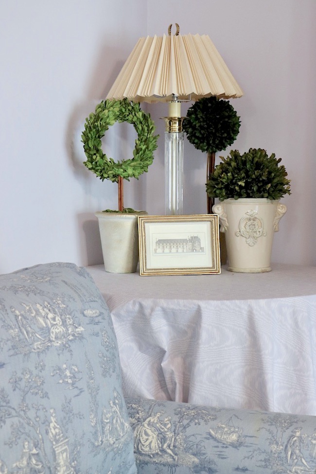 A trio of preserved boxwood topiaries add greenery to the French Country bedroom.