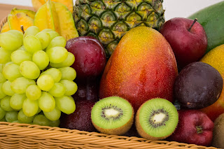 a fruit basket containing various fruits like apple, plums, pineapple, kiwi, grapes, mango