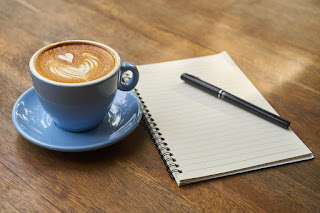 A notebook, pen and cup of coffee on a desk. 