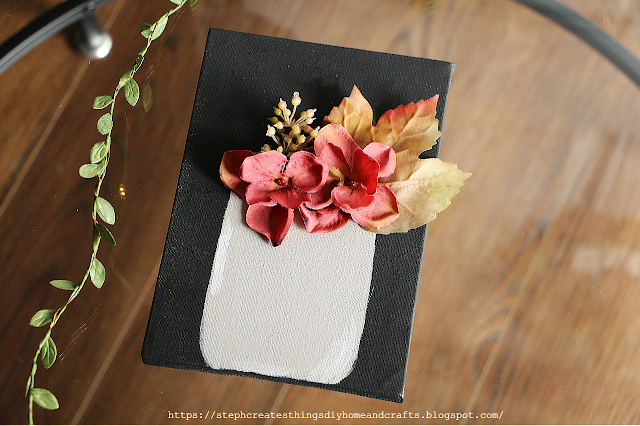 canvas art painted black with faux floral displayed in a painted tan vase