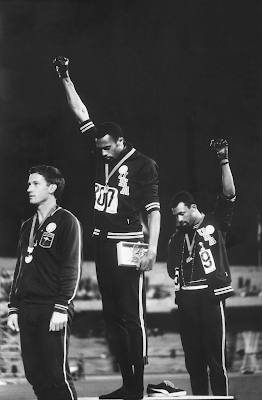 photograph of Tommie Smith (center) and John Carlos (right) raising gloved fists during the medal ceremony for the 200-meters at the 1968 Olympic Games in Mexico City