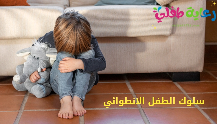 صورة طفل يجلس القرفصاء على الأرض مخفياً وجه وبيده دميته، كتعبير عن سلوك  الطفل الانطوائي.