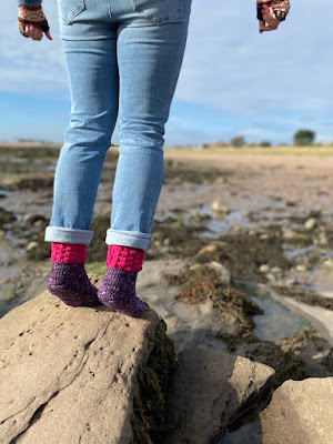 Cropped photo of someone standing on tip-toes at the rock pools. They're wearing jeans and crocheted socks.