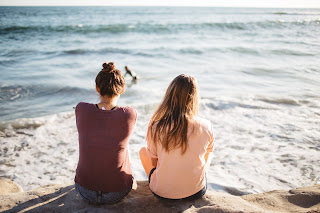 Two people sitting in the sand on the beach | Hearing test near Lansing, MI