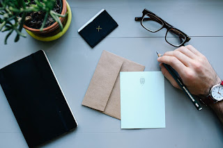 A desk with note paper and a hand with a pen about to write a note.