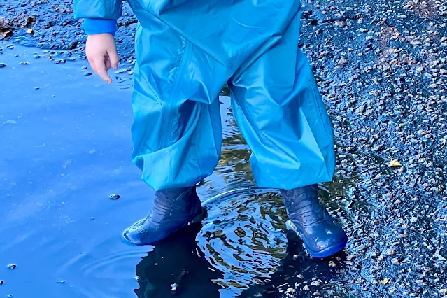 A toddler playing in puddles in a jumpsuit and wellies