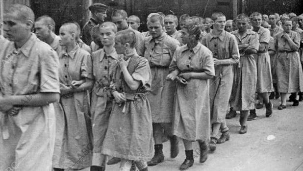 Un grupo de prisioneras a las que se acaba de rapar se dirige al campo de mujeres vigilado por un SS.