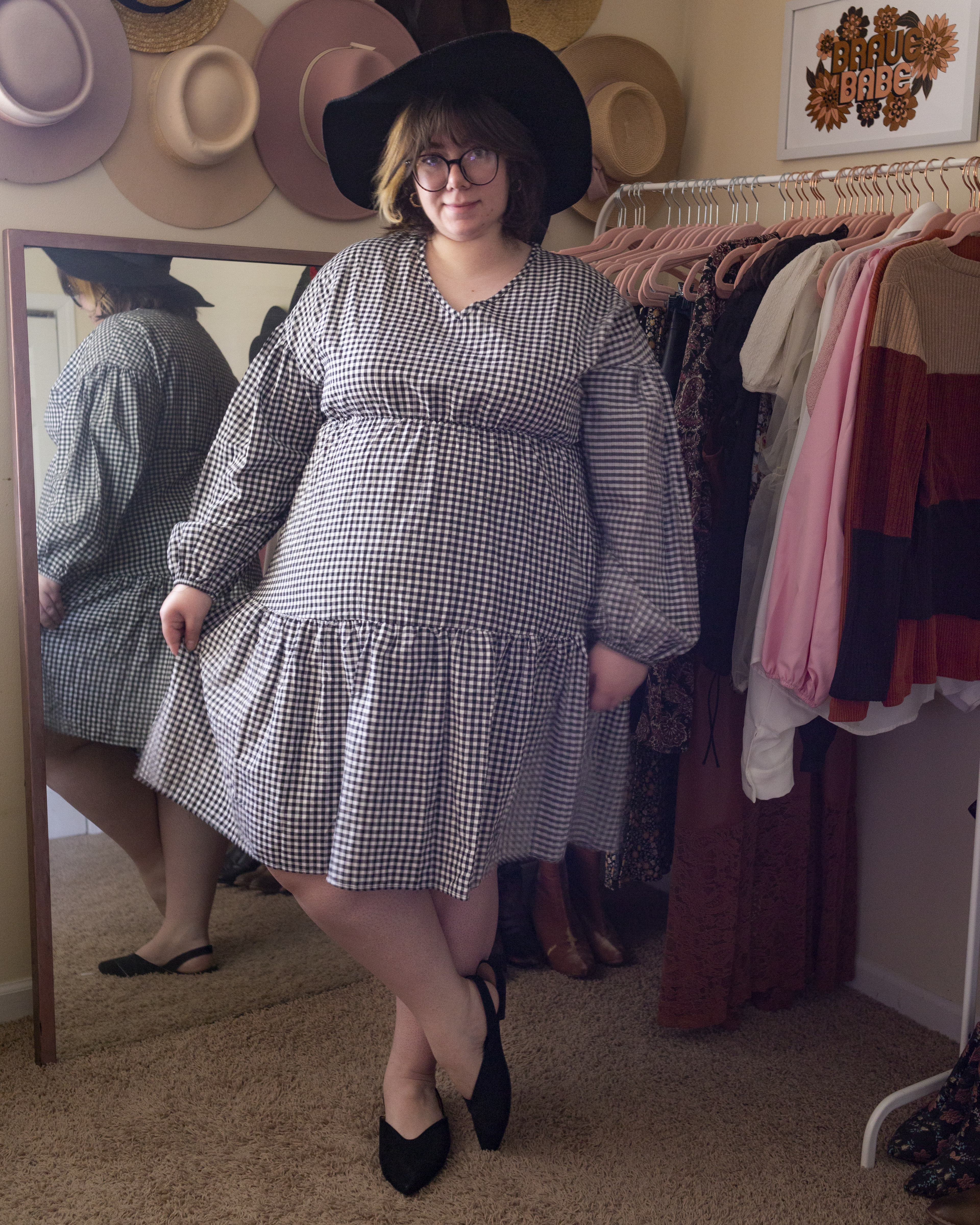 An outfit consisting of a black wide brim fedora, a black and white gingham long bishop sleeve dress and black slingback flats.