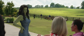 Jen Walters as her six and a half foot tall green She-Hulk form. She's in a pretty blue dress with flowers on it. She's talking with a few of her friends with a pasture in the background.