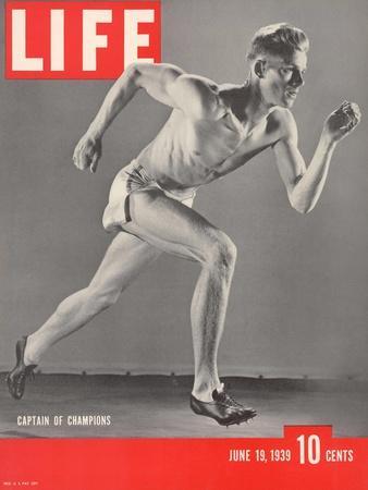 Foto em preto e branco de um atleta em posição de corrida. Ele veste um short e calçados próprios para o esporte.