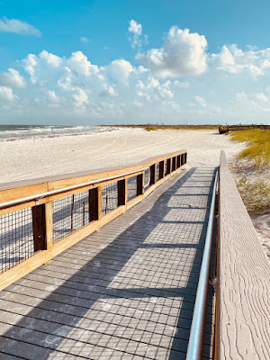 A boardwalk ramp is shown, leading down to the beach. Bright skies and white sand are in the background