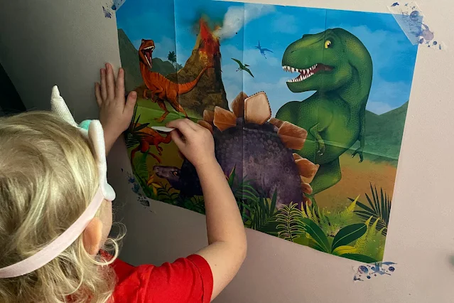 A blindfolded child putting a sticker on a dinosaur