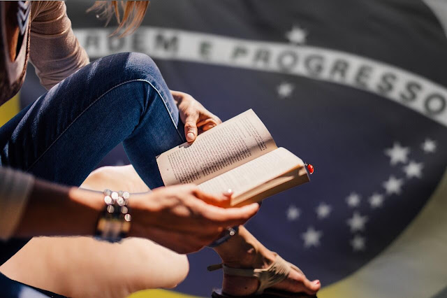 Mulher lendo livro, tendo como fundo o brasão do Brasil.