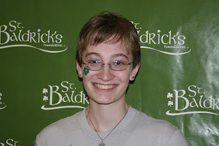 A photo of the blogger, a white woman, with short hair in front of a St Baldricks banner.
