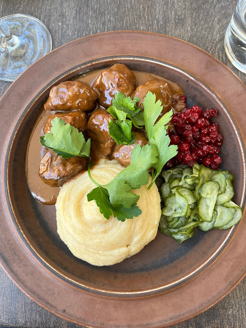 Swedish meatballs, lingonberries, cucumber salad and parsley on a brown plate