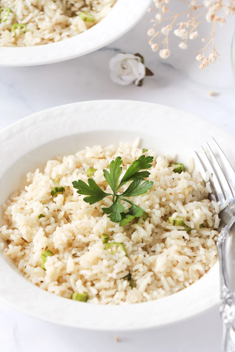 A serving of ochro and rice in a white bowl, garnished with a bunch of cilantro.