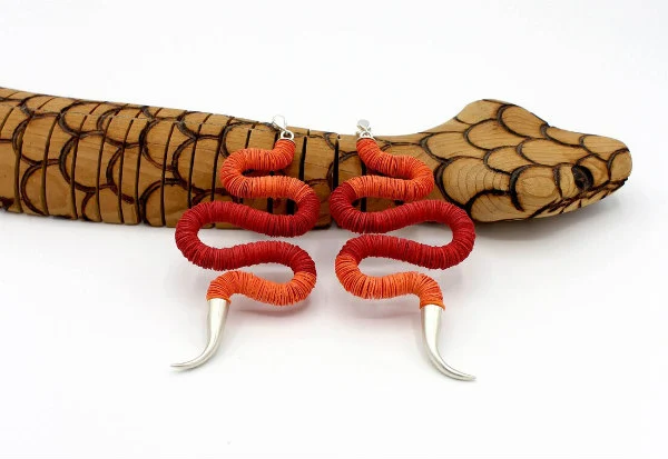 pair of snake-shaped red and orange paper earrings composed of colorful discs displayed on wooden snake.