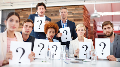 people all gathered around a desk each holding a question mark sign