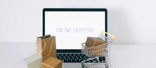 Online shopping sign on a computer screen with shopping bags and a shopping cart in front of the computer screen.