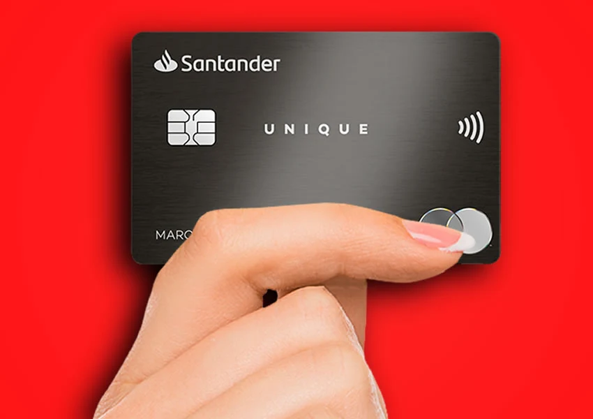A imagem de fundo vermelho mostra uma mão segurando um cartão de crédito santander unique.