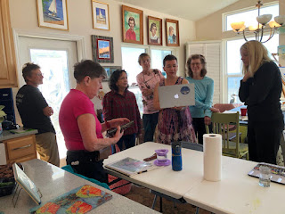 Haley McAndrews, holding a laptop, talking to a small group of women about her artwork.