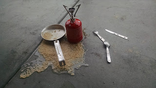 Camp stove, mess kit, and a puddle of oats on the sidewalk
