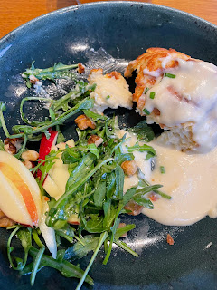 A plate of food. It's half eaten, messy all over the plate, and indecipherable as to what it was. But on the left are the remains if a rocket salad. On the right, the cheese soufflé is squashed, with molten cheese all over the plate. There are walnuts scattered about.