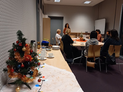 Zdjęcie świątecznego stołu na tle sali z uczestnikami i prowadzącą siedzącymi przy stole.