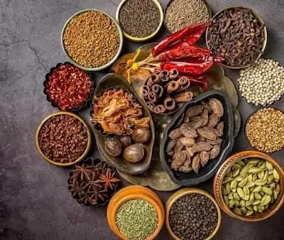 A bowl of homemade garam masala powder surrounded by whole spices like cinnamon, cardamom, and cloves.