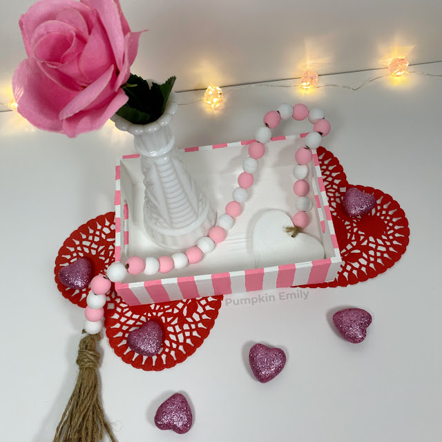 A striped wooden tray with a flower vase and a garland in it.