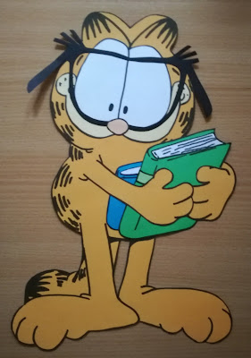 Brązowe tło Garfield w okularach trzymający książki praca plastyczna stworzona  na podstawie książek o Garfieldzie
