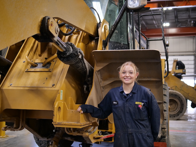 Hailey Brohamer standing in front of a heavy diesel machinery at her job