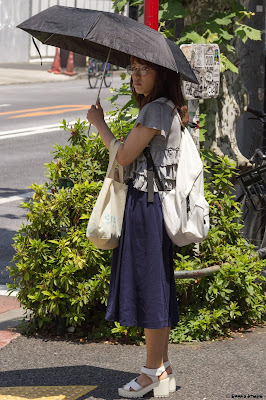 A woman underneath an umbrella on a sunny day in Tokyo.